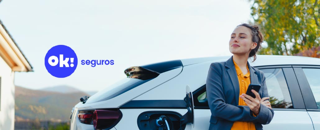 Carro branco elétrico a ser carregado, com o logo da ok! seguros ao lado.